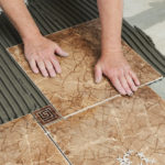 Man placing ceramic floor tile in position over adhesive