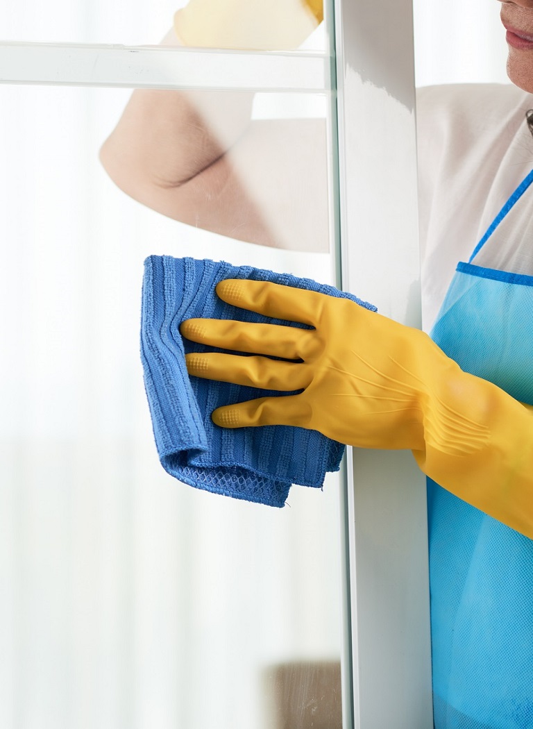 Cropped image of woman cleaning window with rag